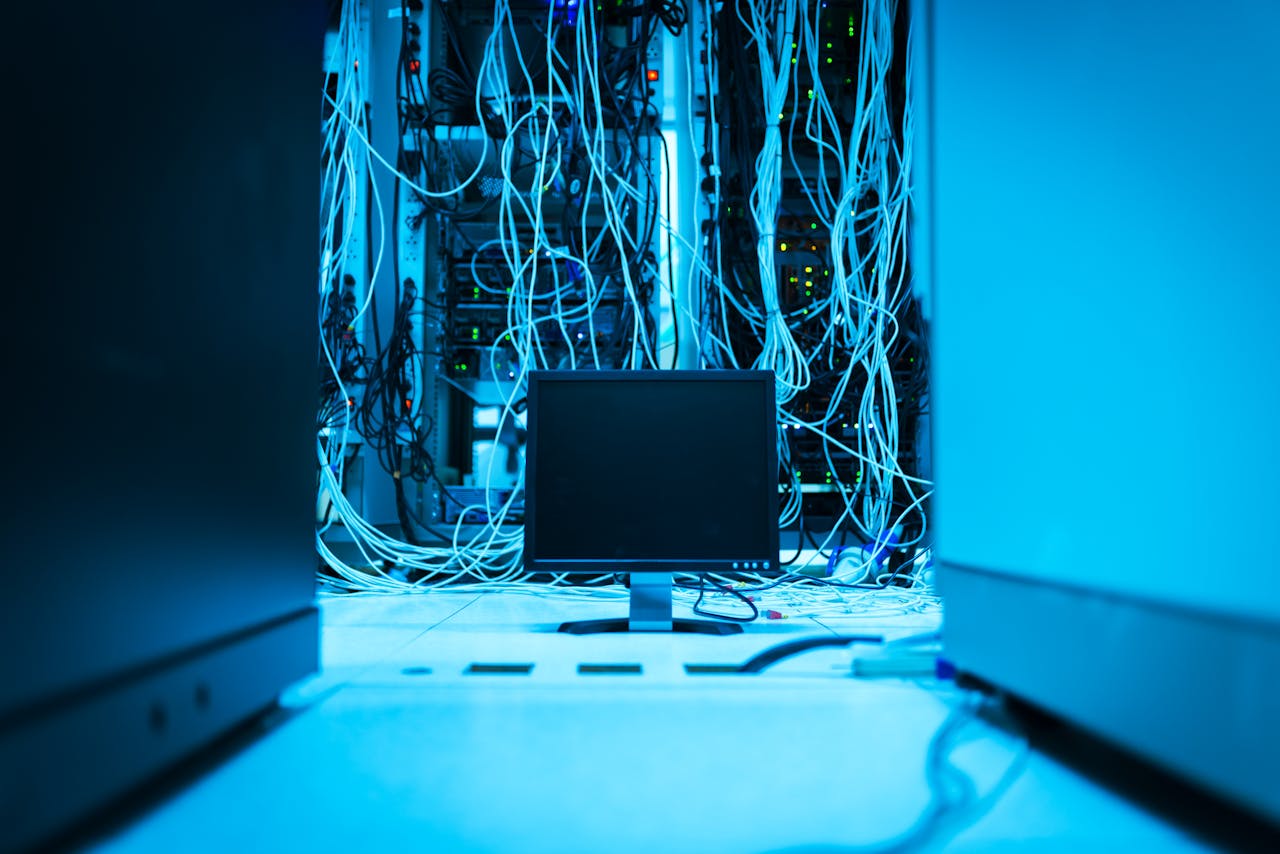 team-01 A complex network of cables in a data center with a monitor in the foreground.